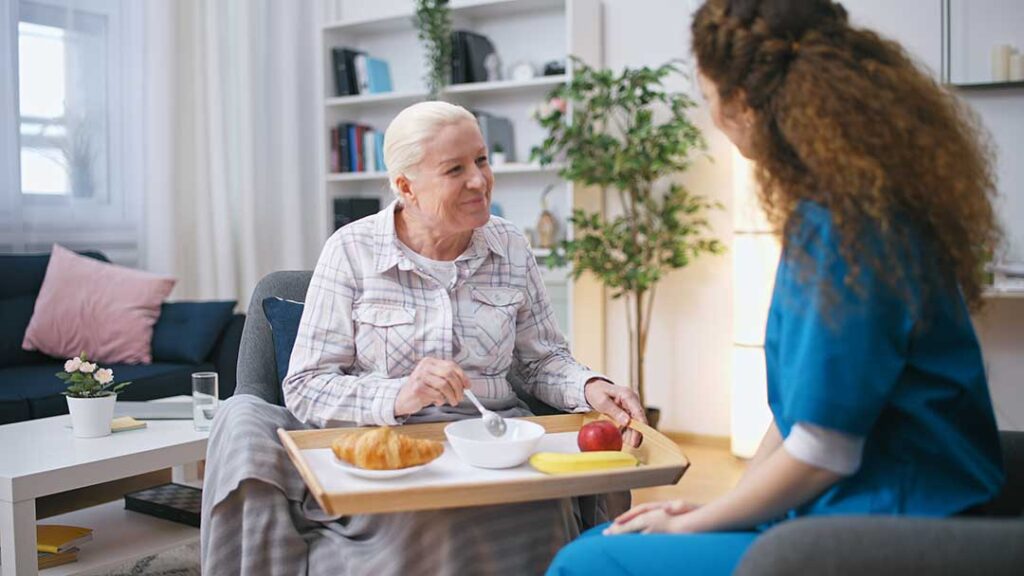 Older adult speaking with a caregiver in a bright assisted living apartment.