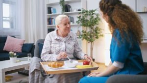 Older adult speaking with a caregiver in a bright assisted living apartment.