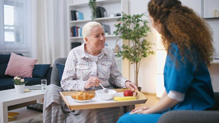 Older adult speaking with a caregiver in a bright assisted living apartment.
